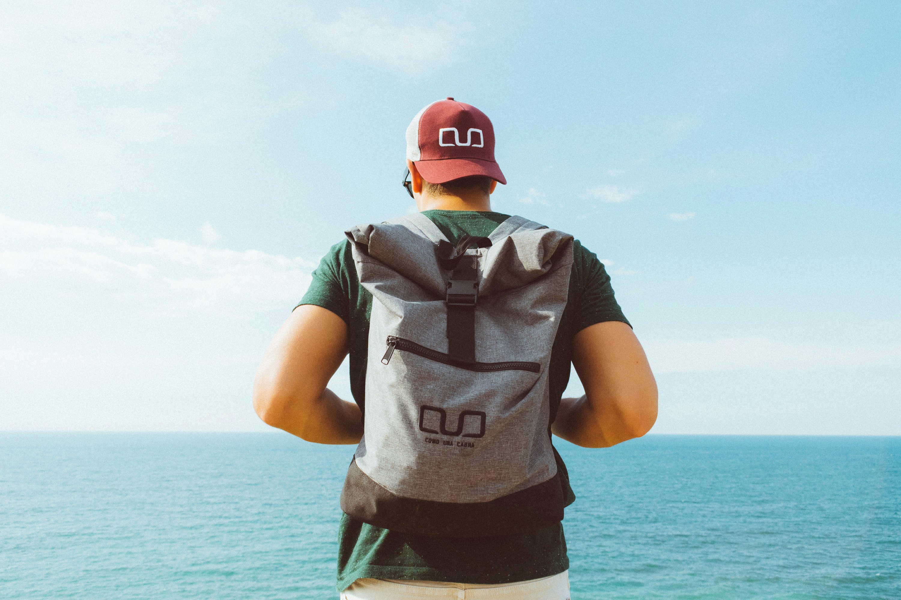 man carrying backpack standing in front of sea